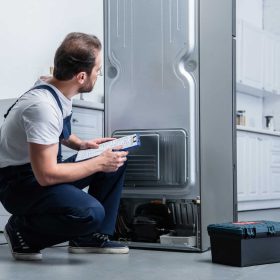 handyman-in-working-overall-writing-in-clipboard-near-broken-refrigerator-in-kitchen.jpg