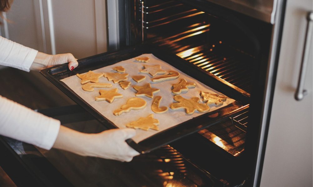 woman putting tray with christmas cookies in oven