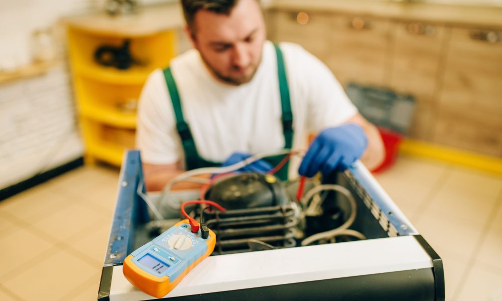 worker in uniform testing refrigerator at home